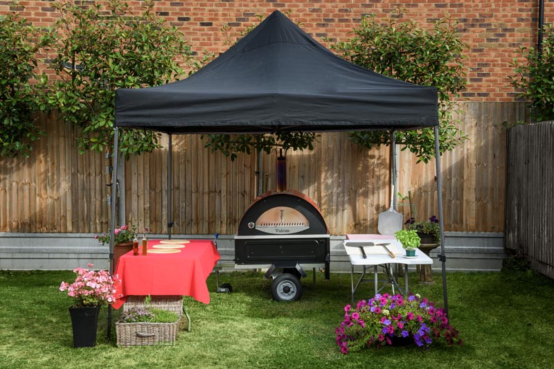 Wood fired pizza oven set up under marquee in garden with service tables